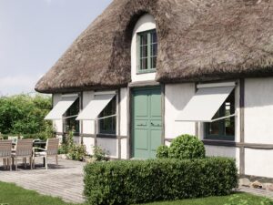 Three Markilux 730 awnings with cream colored fabric and frame attached to a thatched house